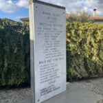 Lapide ai caduti di Piane Crati vista di lato in spazio pubblico con siepe sullo sfondo.