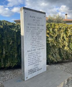 Lapide ai caduti di Piane Crati vista di lato in spazio pubblico con siepe sullo sfondo.